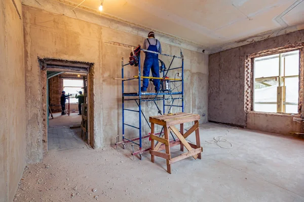 Werknemer is het maken van een technologische gaten voor elektrische cabel in de muur in appartement dat in aanbouw is, verbouwing, renovatie, uitbreiding, restauratie en wederopbouw. — Stockfoto