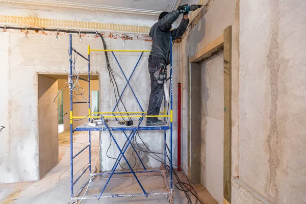 Работник делает технологические отверстия для электрических кабелей в стене в квартире, которая находится в стадии строительства, реконструкции, ремонта, расширения, восстановления и реконструкции. — стоковое фото