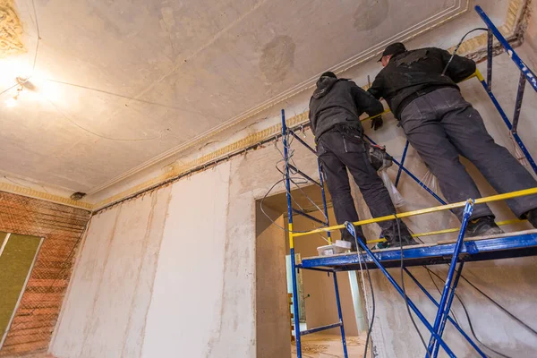 Twee arbeiders is het installeren van de elektrische draden op de muur dat is het deel van de interne bedrading in appartement dat in aanbouw is, verbouwing, renovatie, uitbreiding, restauratie en — Stockfoto