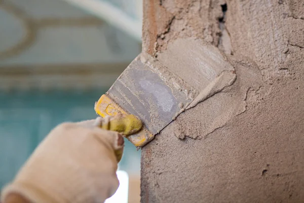 Работник цементирует шпаклевочным ножом стену в помещении, которое находится в стадии строительства, реконструкции, реконструкции, расширения, реставрации и реконструкции. Эффект фокусировки на рабочих руках. — стоковое фото