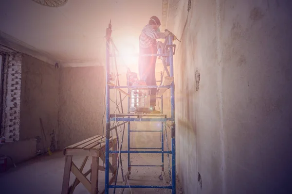 Arbeiter macht ein technologisches Loch für elektrische Kabel in der Wand in der Wohnung, die im Bau ist, Umbau, Renovierung, Erweiterung, Restaurierung und Wiederaufbau. — Stockfoto