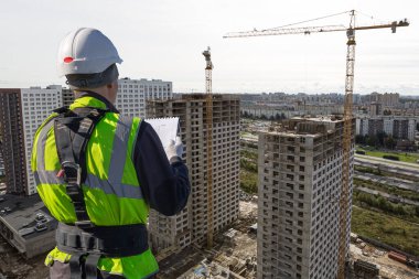 Miğferli ve üniformalı inşaat işçilerinin kolajı teknik dökümanları ve inşaat alanını okuyor.