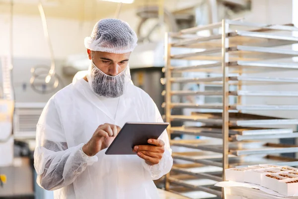 滅菌均一性の監督者は食品工場に立っており 生産性をチェックするために彼のタブレットを使用しています — ストック写真