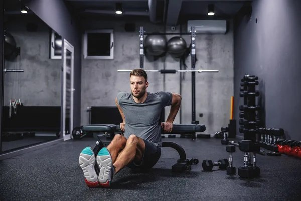 A male athlete does triceps push-ups on a sports bench workout in a modern gym. The concept of fitness training, sports, pumping arm muscles, press ups