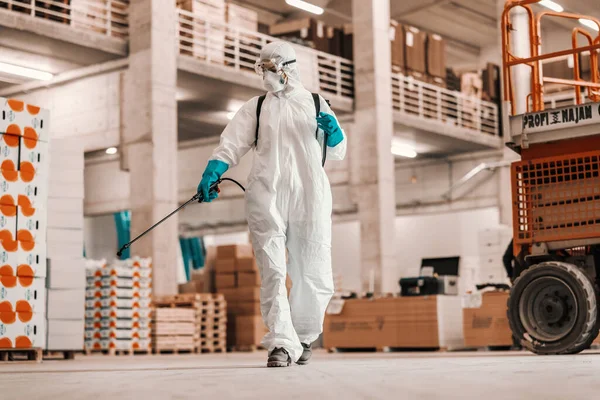 コロナウイルスとの深刻な状況 保護白いスーツの人によるCovid19の抑制と工場倉庫内の清掃場所 クリーニング噴霧器 滞在保護 コロナの状況 — ストック写真