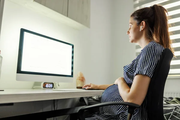 怀孕妇女和电脑 准备为人父母 一个大肚子的女人坐在电脑前 耳朵里拿着耳机 用鼠标在网上授课 怀孕的女商人 — 图库照片