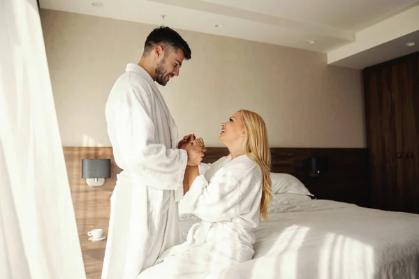 子供のいないロマンチックな週末穏やかなタッチで目を覚ますとホテルの部屋でキスストレスの多い週後に正のエネルギーでいっぱいの豪華なスパホテルの美しいカップルバスローブで快適 — ストック写真