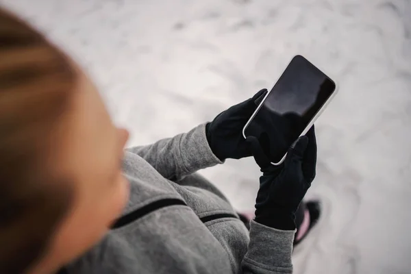 Hands holding smart phone. Close up of woman holding phone while standing in nature on snow. Telecommunications, technology, social media