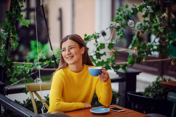 Uśmiechnięta Młoda Kobieta Siedząca Tarasie Kawiarni Trzymająca Filiżankę Kawy Odwracająca — Zdjęcie stockowe