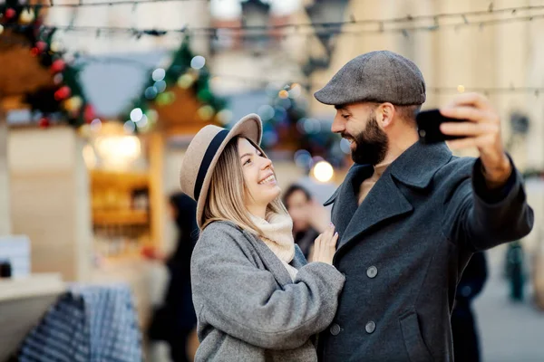 クリスマスカップルは新年に屋外で自撮りします 通りに立って笑って抱きかかえて自撮りしている若い幸せなカップル — ストック写真