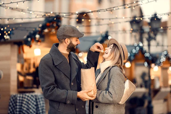 クリスマスは新年の通りのポップコーンと供給する愛好家 幸せな若い男は彼の最愛のガールフレンドと路上に立っていると彼女のポップコーンを食べます元旦 — ストック写真