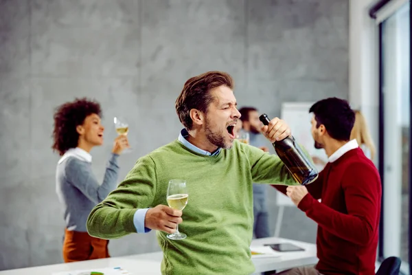 仕事で成功を祝うビジネスマン 幸せなビジネスマンが成功と昇進のためにオフィスでガラスとシャンパンとダンスのボトルを保持しながら 彼の同僚が楽しみを持っている背景に — ストック写真