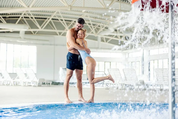 水着を着た幸せなカップルは スパセンターの暖かい水でプールの隣に立っています 夫婦は抱き合って一緒に時間を楽しんでいます スパとウェルネスセンターでカップル — ストック写真