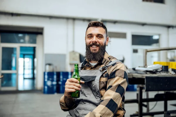 Trabalhador Barbudo Feliz Macacão Está Sentado Oficina Segurando Uma Cerveja — Fotografia de Stock