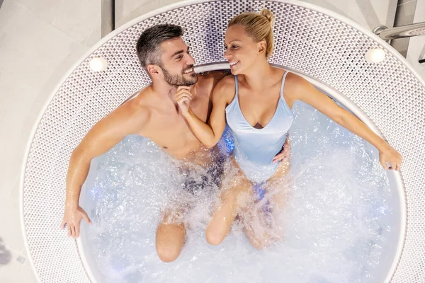 Top view of a happy attractive couple hugging and sitting in a hot tub. Happy couple spending the weekend at the resort. Couple in the hot tub at spa center