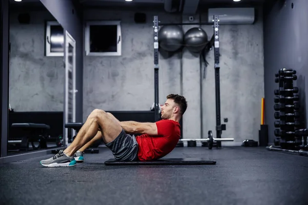 The importance of breathing during training. A handsome young male person performs abdominal exercises and sighs properly and exhales. Healthy fitness habits and sports routines. Modern indoor gym