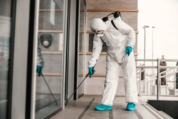彻底消毒酒店透明入口的门 一个穿着白色防护服 蓝色手套和橡胶的男人的照片 Coronavirus站点 旅行安全 — 图库照片