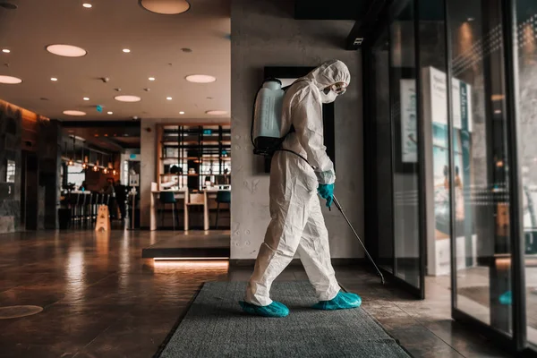 Sanitation of the hotel entrance. A man in a protective suit sprays chemicals at the entrance of the hotel. Covid free space, Corona alert situation