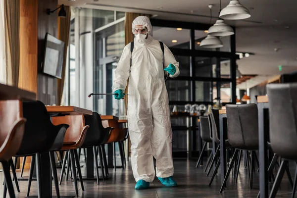 自然光のある屋内レストランでのコロナウイルスの消毒 感染症の抑制 化学ノズルで保護服の男性による空間の殺菌 Covid19 — ストック写真