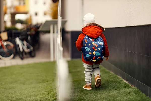 Rear view of a kindergarten child with schoolbag on his backs walking outdoors.