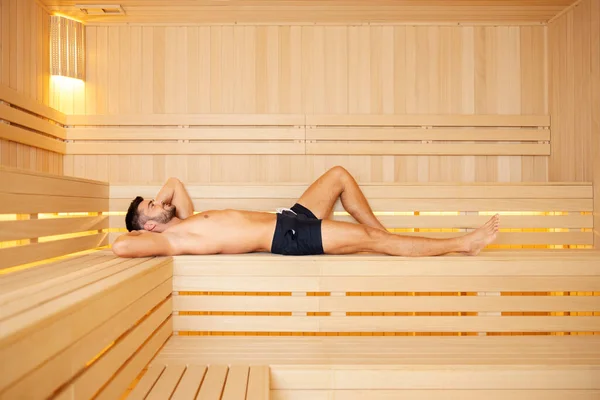 A healthy man lying in the sauna. A happy handsome muscular man lying down in a sauna and relaxing.