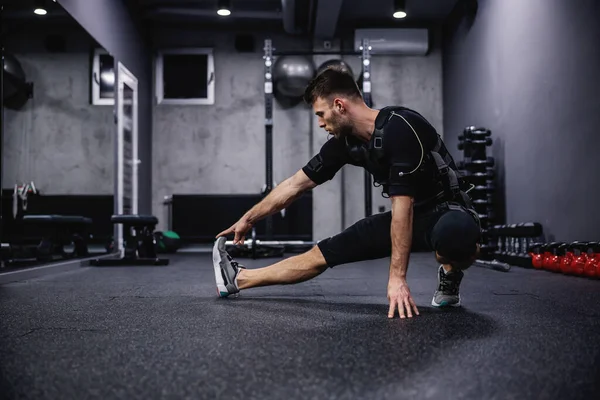 Jovem Desportista Num Fato Ems Especial Alonga Pernas Aquece Músculos — Fotografia de Stock