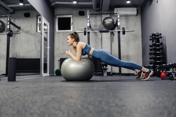 Plank position elbows resting on a fitness ball. A fit and slim woman in sportswear does exercises to strengthen the muscles of the whole body. Female is in the plank position for endurance exercises