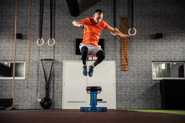 Powerful, dynamic and strong movement of a person in individual fitness training. A strong man in sportswear jumps high on the modern gym concept. The athlete exercises indoor sports hall