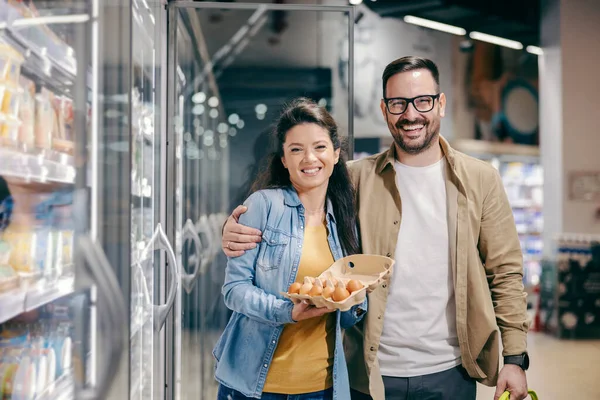 Pareja Abrazando Sosteniendo Huevos Frescos Supermercado Sonriendo Cámara —  Fotos de Stock