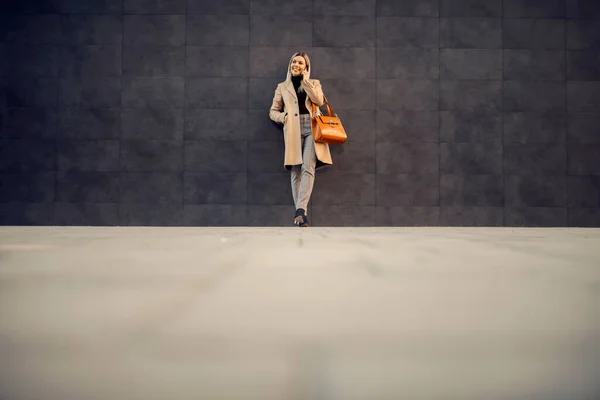 一个穿着外套的时髦女人靠在外面的墙上 在电话里聊天 — 图库照片