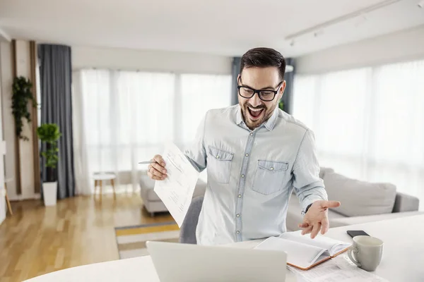 Hombre Emocionado Sosteniendo Papeleo Mirando Portátil Acogedora Casa — Foto de Stock