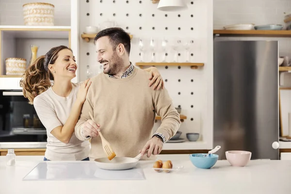 彼らの居心地の良いアパートでキッチンで朝食のための卵を作る幸せなカップル — ストック写真