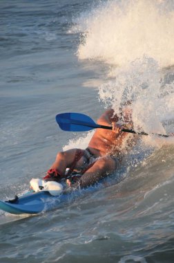 Kayaker paddling and riding a wave in the ocean.