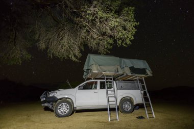 Bir safari macerası sırasında Afrika çalılıklarında çadırı olan Offroad 4X4 arabası. Çatı çadırıyla kamp yapmak. Gece vakti..