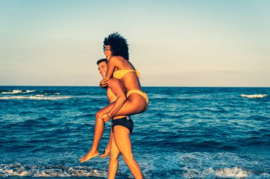 Sahilde eğlenen neşeli Afro-Amerikalı kız arkadaş plaj tatillerinde aşık olan mutlu çoklu etnik çift genç erkek arkadaşından beslenen neşeli çok ırklı kız.