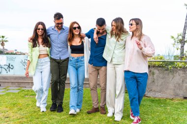 Gençler güneşli bir günde, şehir parkında gezerken - arkadaşlık ve mutluluk kavramı - karışık ırktan çok kültürlü insanlar, renkli kıyafetler giyip birlikte eğleniyorlar.