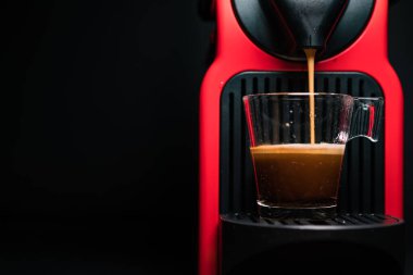 Kahve makinesiyle kahve makinesini cam şeffaf fincana çevirme işlemi - otomatikleştirilmiş kahve makinesinden çıkan espresso kahvesi - stüdyoda çok az izole edilmiş - siyah arka planda.