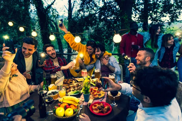 Young people dining and singing with phone flashlight on  group friend having fun drinking wine in dinner party  dinning and drinking on terrace restaurant  happy people eating food together