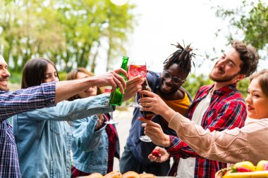 Çoklu etnik çeşitliliğe sahip gençler havuz başında kadeh kaldırırken çok ırklı grup arkadaşları açık havada sosyal kapılar ardında birlikte içerken eğleniyorlar.