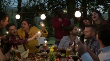 Çok ırklı genç insanlar ellerinde el feneriyle cep telefonu tutarak şarkı söylüyor. Çatıdaki terasta eğlenen çok ırklı gençler parti şarkıları söylüyorlar.  