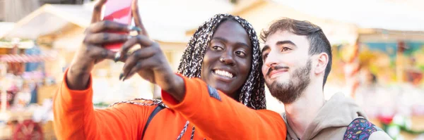 Happy multiethnic couple in the city taking photo - Smiling man and african girl taking selfie with smartphone on street  multiracial Happy couple having fun taking a selfie  banner size for header