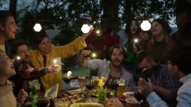 Çok ırklı genç insanlar ellerinde el feneriyle cep telefonu tutarak şarkı söylüyor. Çatıdaki terasta eğlenen çok ırklı gençler parti şarkıları söylüyorlar.  