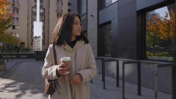 Joven adulto asiático mujer de negocios caminando en un soleado día de otoño dorado con una taza de café — Vídeos de Stock