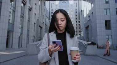 Asyalı iş kadını ofisten çıkarken telefonunu karıştırıyor.