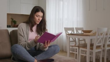 20 'li yaşlarda beyaz bir kadın evdeki akıllı bir telefondan notlarını kontrol ediyor.