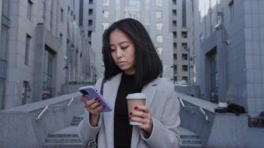 Asyalı bir kadın şehrin dışındaki akıllı telefonunda geziniyor.