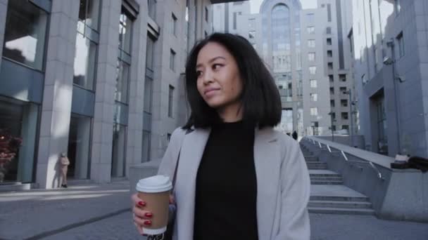 Впевнена молода доросла азіатська бізнес-леді йде своїм шляхом з кавою в офісному центрі — стокове відео