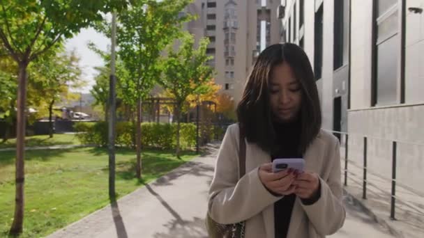 Genç Asyalı kadın şehirde yürürken akıllı telefonuyla çalışıyor. — Stok video