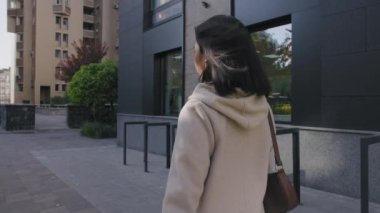 Genç, Asyalı bir kadın güneşli bir sonbahar gününde şehir sokaklarında yürüyor.