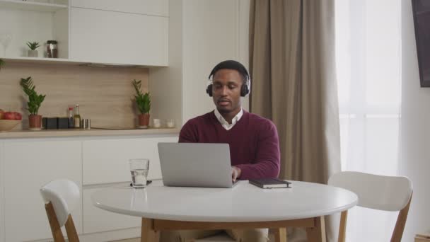 Широкий знімок молодого афроамериканського чоловіка в навушниках, який працює на ноутбуку. Закробат кол-центру, що працює далеко — стокове відео